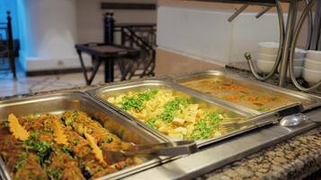 A buffet with various dishes, including what appears to be a meat dish garnished with herbs, a vegetable dish, and a pasta dish.