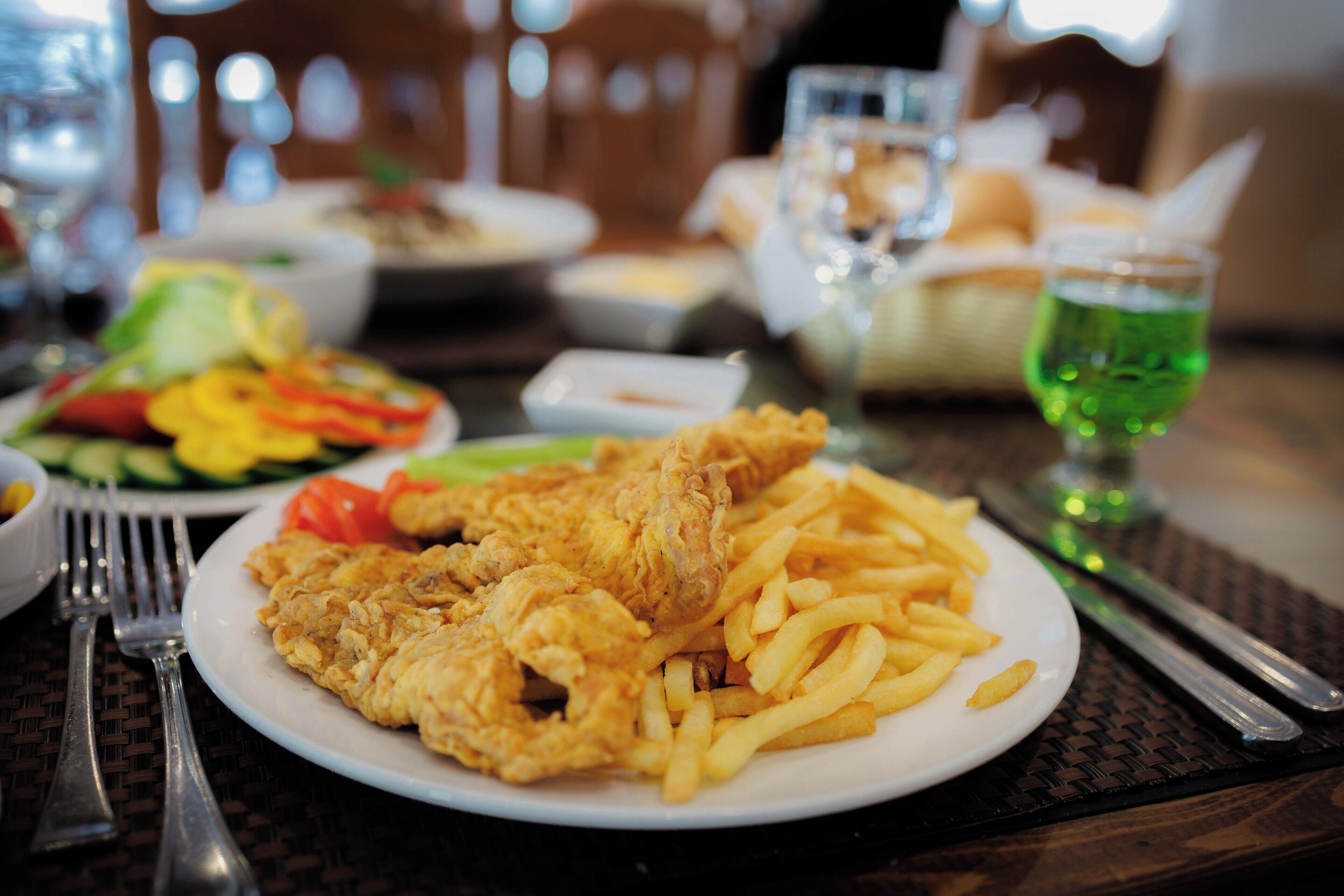 Uma mesa de jantar com um prato de frango frito e batatas fritas, uma salada e um copo de bebida verde.