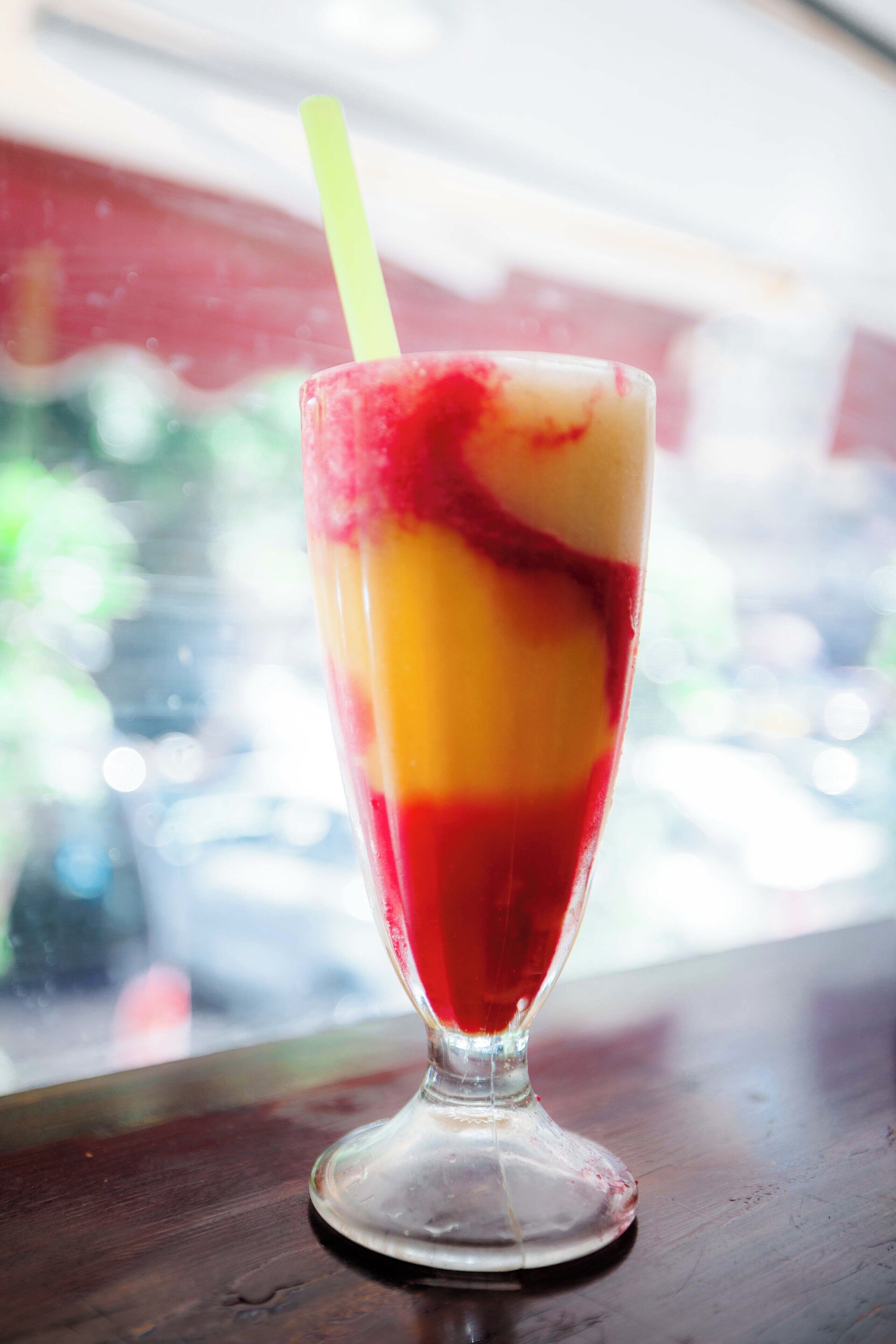 Bebida postre en capas en un vaso con pajita, sobre una superficie de madera.