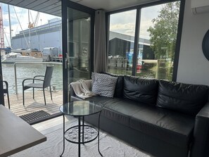 Ein modernes Zimmer mit Glaswand, einer schwarzen Ledersofa, einem kleinen runden Tisch und einem Sessel.