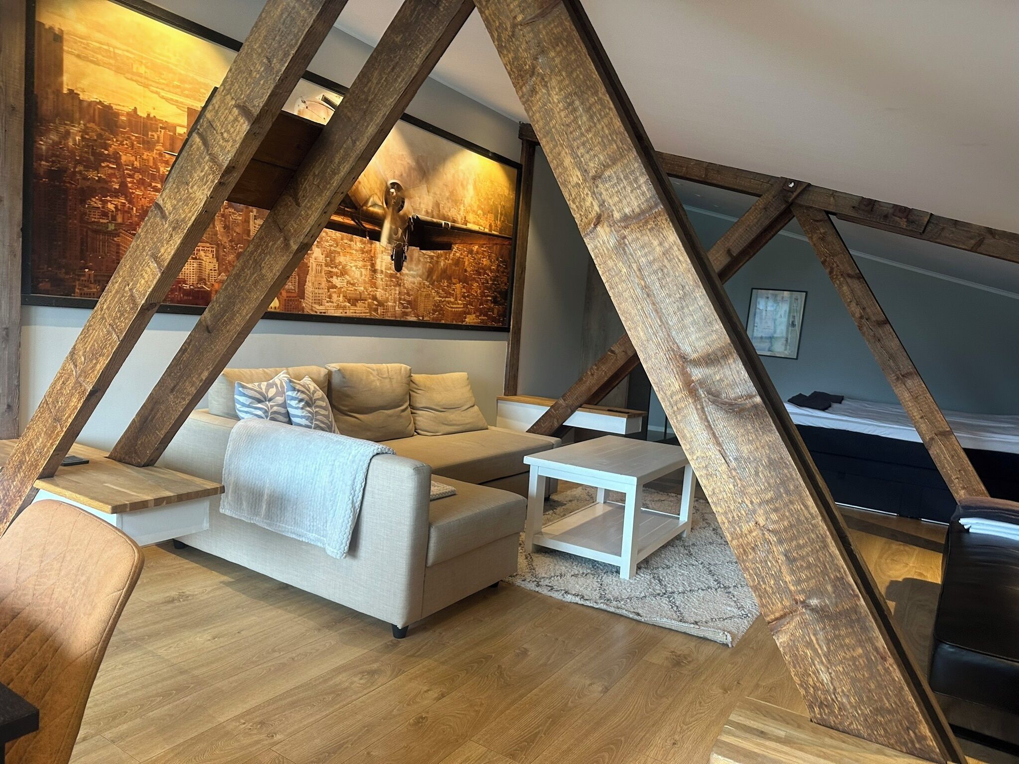 Una habitación estilo loft con vigas de madera a la vista, un sofá, una mesa de centro y un mural con vistas urbanas en la pared.