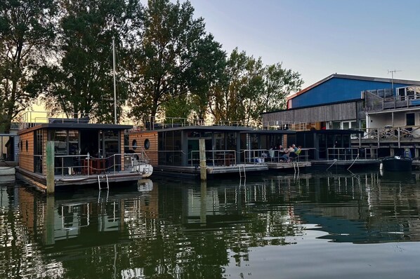 A waterfront property with docked boats, a wooden building with a deck, and a blue building with a balcony. - La Mare Resort (Gothenburg)