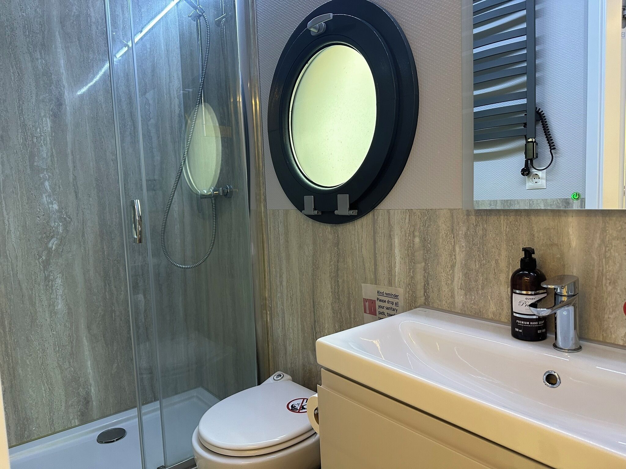 Une salle de bain avec une douche à parois de verre, des toilettes, un lavabo avec un distributeur de savon et un miroir.