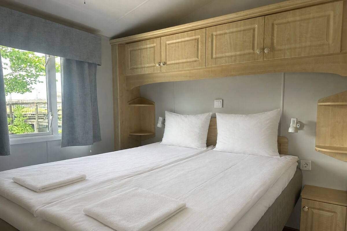 A double bed with two pillows, a bedside table, a nightstand, and a window with curtains.