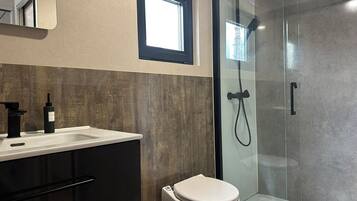 A modern bathroom with a glass-enclosed shower, a white toilet, and a sink with a black faucet.