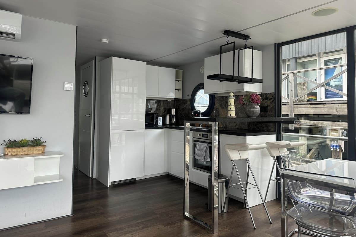 A modern kitchen with white cabinets, a built-in oven, and a dining area with a glass table and chairs.