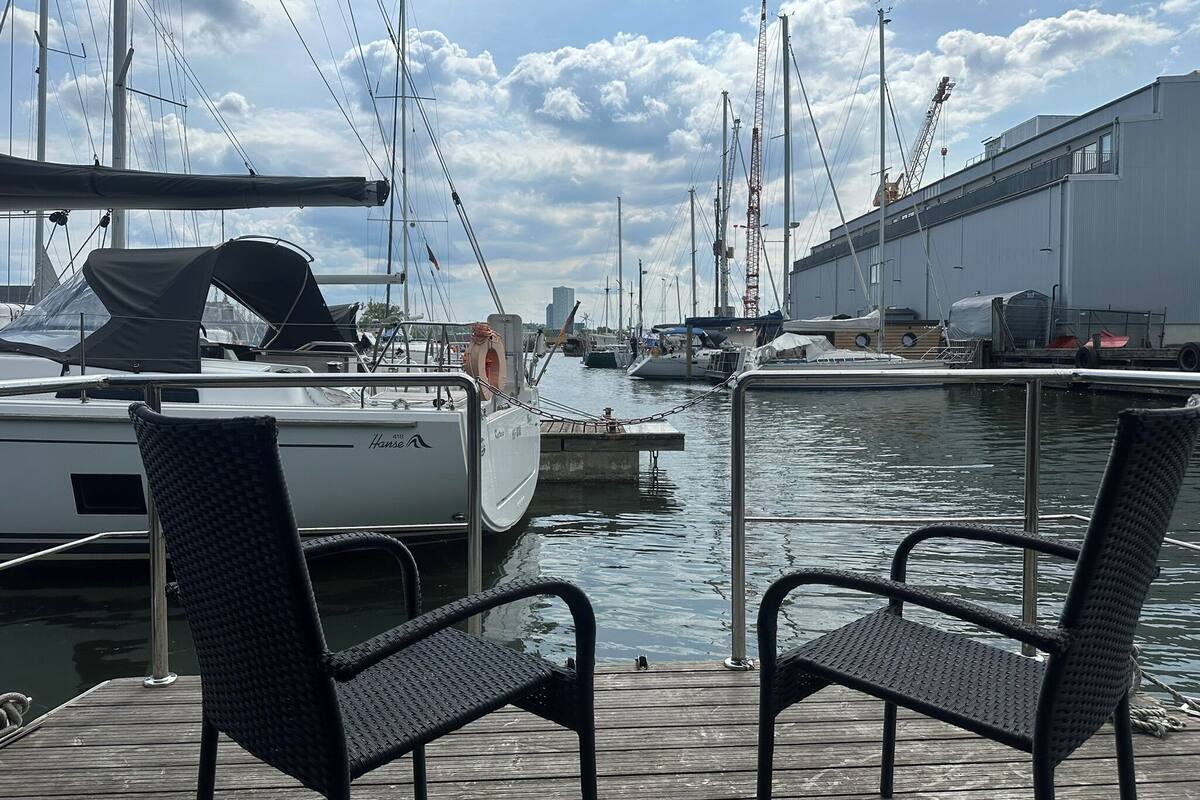A marina with docked sailboats, a wooden deck, and two wicker chairs.