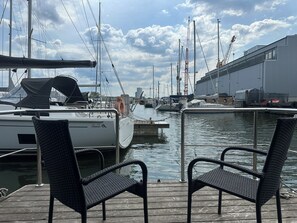 Ein Yachthafen mit vertäuten Segelbooten, einem Holzboden und zwei Korbstühlen.