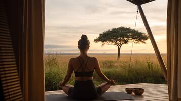 Eine Person sitzt auf einer Yogamatte im Freien, mit Blick auf einen Baum und ein offenes Feld.