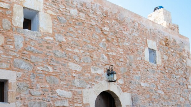 A stone building with a central arched doorway, a small window, and a lantern above the door.