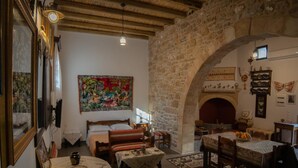 A traditional room with a stone wall, a bed, a table with a bowl, and a fireplace.