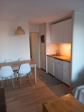 Une cuisine moderne avec des armoires blanches, un comptoir en bois et un lave-vaisselle encastré. On y trouve également un coin repas avec une table en bois et des chaises blanches.