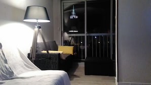 Ett sovrum med en säng, ett nattduksbord, en lampa och ett fönster med utsikt över omgivningen.