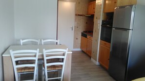 A compact kitchen with a dining table and chairs, wooden cabinets, and a stainless steel refrigerator. - Le Cosmos, apartment near the beach (Agde)