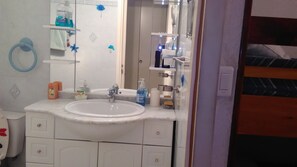 A bathroom with a white sink, mirror, and various toiletries. There is a towel ring on the wall and a shower curtain rod visible. - Le Cosmos, apartment near the beach (Agde)