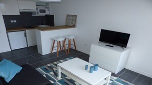 Um espaço compacto com cozinha compacta, TV em um suporte, sofá e mesa de centro.
