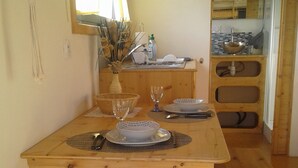 A wooden dining table with a bowl, glasses, and plates set for two. A small cabinet with a sink and a mirror is in the background. - Tiny House on the Presqu'île Sauvage (Lanmodez)