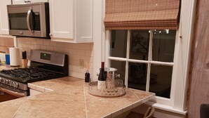 A kitchen with white cabinets, a microwave, a stove, and a large island with chairs. - Darby's Guest House! (Natchez)