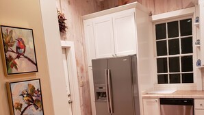A kitchen with wooden flooring, white cabinets, a stainless steel refrigerator, and a dishwasher. - Darby's Guest House! (Natchez)