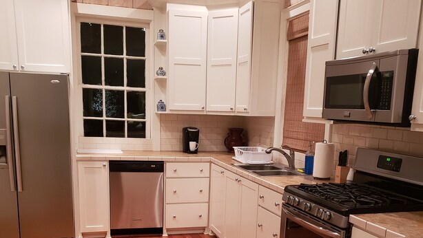A kitchen with white cabinets, a stainless steel refrigerator, a dishwasher, a stove, and a microwave. - Darby's Guest House! (Natchez)