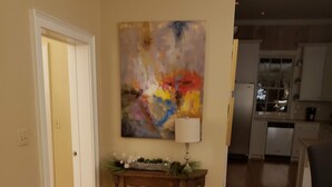 A living room with a wooden floor, a table with a lamp, and a colorful abstract painting on the wall. - Darby's Guest House! (Natchez)