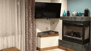 Una sala de estar con televisor de pantalla plana, chimenea, banca de mimbre y un taburete redondo.