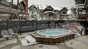 Un jacuzzi rodeado de árboles cubiertos de nieve y una valla de madera.