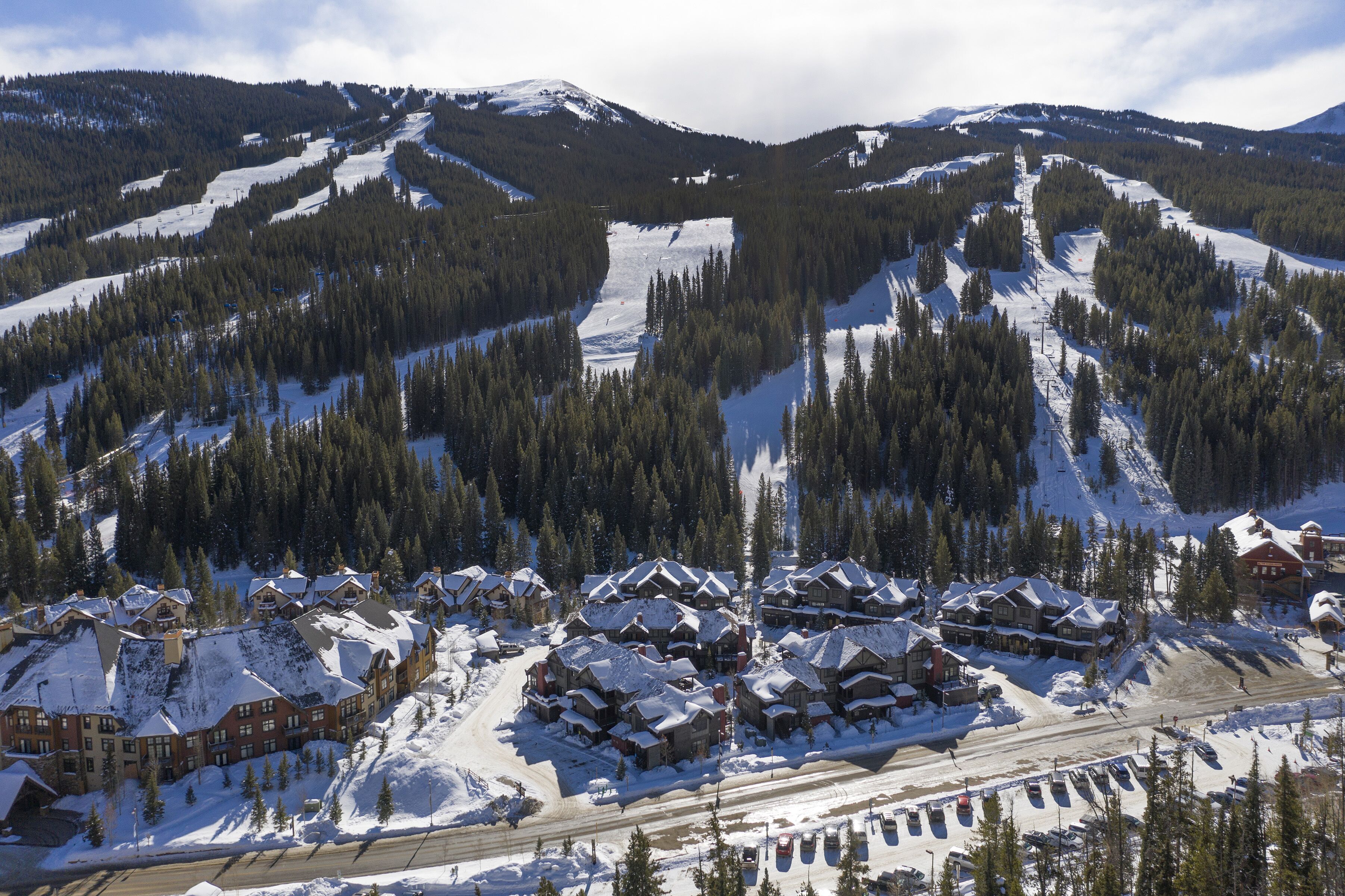 Een skigebied met meerdere gebouwen, besneeuwde wegen en beboste bergen eromheen.