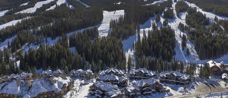 Een skigebied met meerdere gebouwen, besneeuwde wegen en beboste bergen eromheen.