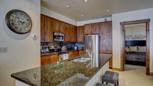 Una cocina moderna con encimeras de granito, electrodomésticos de acero inoxidable, armarios de madera y un microondas integrado.