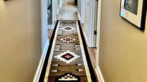 A hallway with a patterned rug, framed pictures on the walls, and a wooden door at the end. - Pueblo Courtyard Home on Rail Trail (Santa Fe)