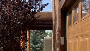 A garage door, a concrete pathway, and a tree with red leaves. - Pueblo Courtyard Home on Rail Trail (Santa Fe)