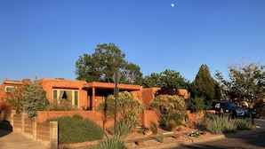 A modern house with a red exterior, surrounded by a landscaped garden with various plants and trees. - Pueblo Courtyard Home on Rail Trail (Santa Fe)