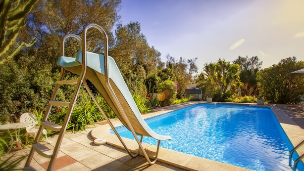 Una piscina con tobogán, rodeada de vegetación y un cielo despejado.