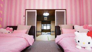A room with two beds, each with pink bedding and Hello Kitty plush toys. There is a small window with a view of the outside.