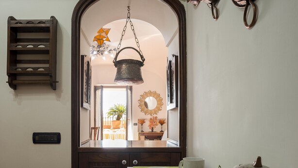 An arched doorway leading to a dining area with a hanging basket, a wall-mounted mirror, and a small shelf.