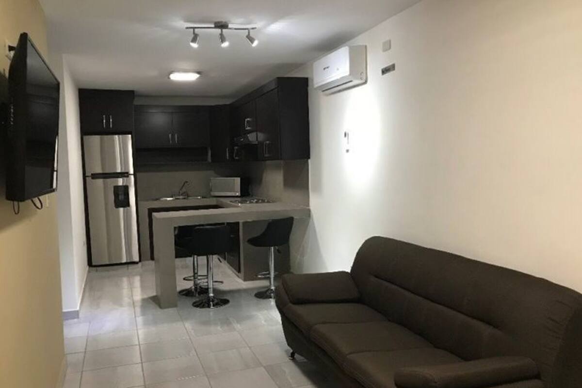 A compact kitchen with dark cabinets, a stainless steel refrigerator, and a central island with bar stools.