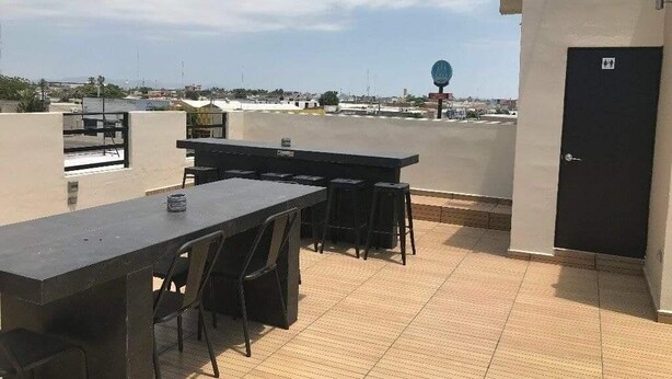 A rooftop terrace with a long table and chairs, a door, and a view of the cityscape.