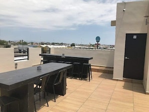 A rooftop terrace with a long table and chairs, a door, and a view of the cityscape. - Departamentos Enki Centro (Cajeme)