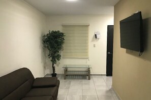 A room with a sofa, a glass-top table, a potted plant, a television mounted on the wall, and a door. - Departamentos Enki Centro (Cajeme)