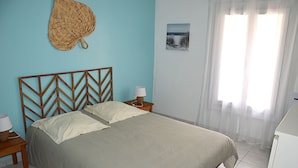 Une chambre à coucher comprenant un lit, une table de chevet, une lampe, un panier fixé au mur et une fenêtre avec des rideaux.