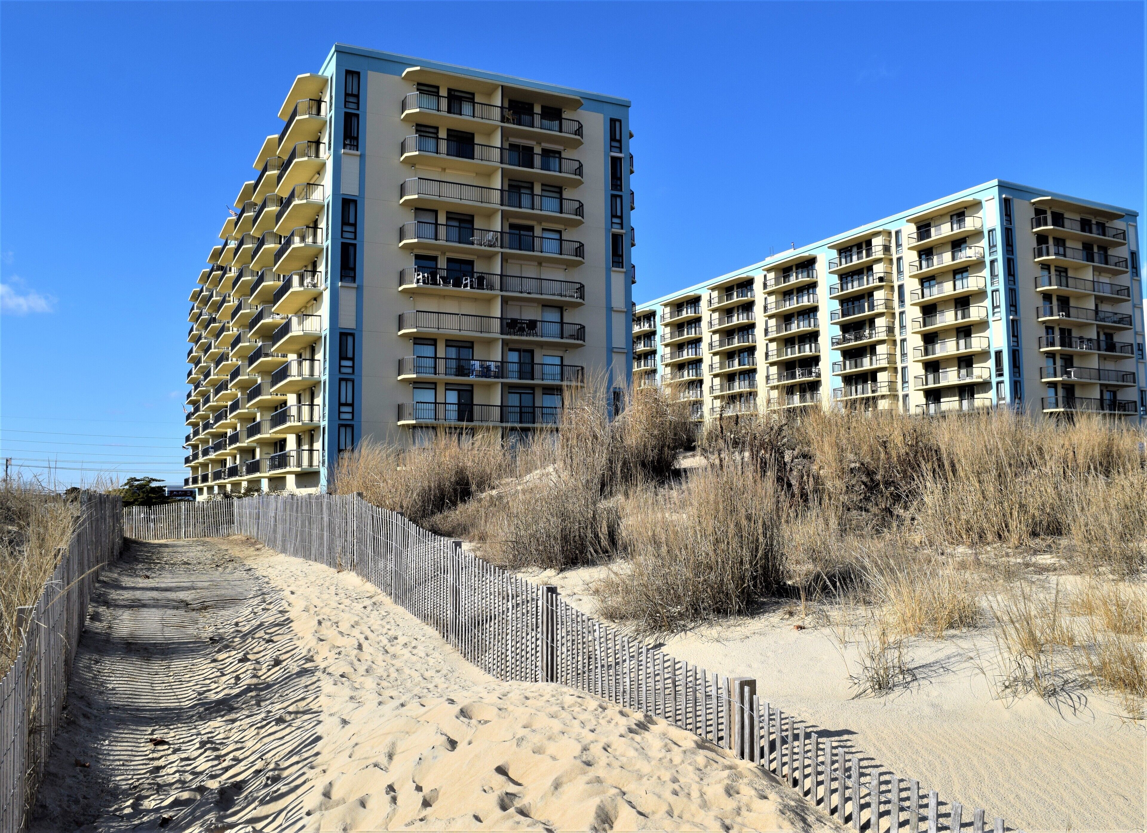A beachfront hotel with multiple balconies and a sandy walkway leading to the beach.