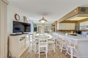 A modern kitchen with a central island, white cabinetry, and a flat-screen TV.