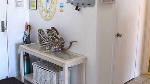A room with a white wall, a framed picture, a wall-mounted mirror, a small table with baskets, and a door. - LINENS & DAILY ACTIVITIES INCLUDED! Braemar -1BR - Pool, Tennis & Fitness Center (Ocean City)