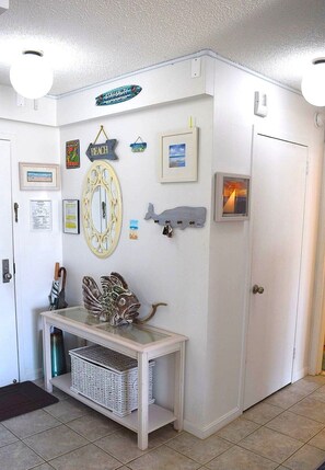 A room with a white wall, a framed picture, a wall-mounted mirror, a small table with baskets, and a door.