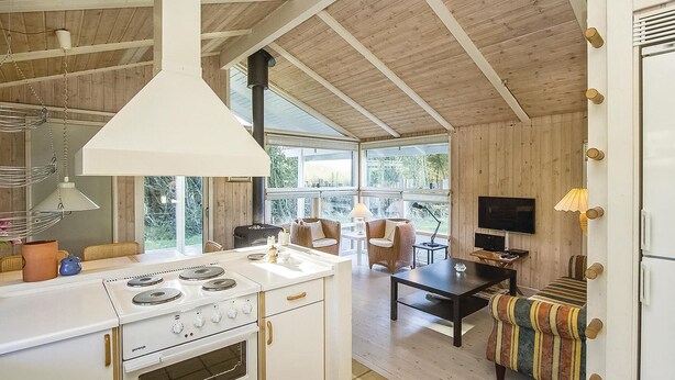 A modern kitchen with a stove, oven, and dining area with wicker furniture. - Cozy home in Blokhus with WiFi (Blokhus)