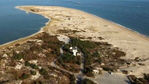 Vue aérienne d’une zone côtière avec une plage de sable, un petit bâtiment blanc et une route menant à ce bâtiment.