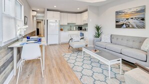 Un salon moderne avec un canapé gris, une table basse et un coin repas comprenant une table et des chaises blanches.