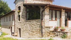 A stone building with a sloped roof, large windows, and a small porch area with potted plants.