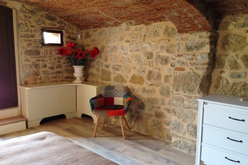 A rustic room with stone walls, a wooden floor, a white dresser, and a colorful chair.